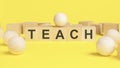 text TEACH on wooden cubes. bright yellow surface. wooden sphere balls among the wood cubes, TEACH - short for Teacher