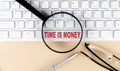 Text TIME IS MONEY on keyboard with magnifier , glasses and pen on beige background