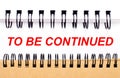 Text TO BE CONTINUED on white paper between white and brown spiral notepads