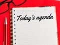 Text Today`s agenda on note book with pen and eye glasses  on red background. Royalty Free Stock Photo