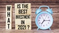 Text What is the best investment in 2021 on wooden blocks and alarm clock on wooden background.