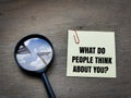 text What do people think about you on sticky note with magnifying glass on wooden background. Royalty Free Stock Photo