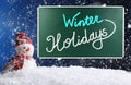 Text Winter Holidays on school chalkboard against decorative snowman in snowdrift