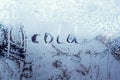 Text word cold on frosty glass covered with white frost crystals on window on winter cold clear morning