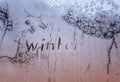 Text word winter scraped on frosty glass covered with white frost crystals on car blue window on winter cold clear morning Royalty Free Stock Photo