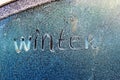 Text word winter scraped on frosty glass covered with white frost crystals on car blue window on winter cold clear morning Royalty Free Stock Photo