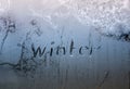 Text word winter scraped on frosty glass covered with white frost crystals on window on winter cold clear morning