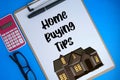 Text written Home buying tips and cartoon of house at white paper on clipboard, pen, glasses and calculator isolated Blue Royalty Free Stock Photo