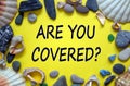 Text `are you covered` on a beautiful yellow background. Sea stones and seashells. Travel insurance concept Royalty Free Stock Photo