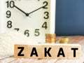 Text ZAKAT on wooden cubes with blurry rice grain,coins and alarm clock on wooden table. Royalty Free Stock Photo