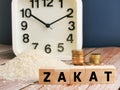 Text ZAKAT on wooden cubes with blurry rice grain,coins and alarm clock on wooden table. Royalty Free Stock Photo