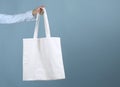 Textile eco bag in woman`s hand,person holding fabric tote on blue background empty copy space