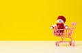 Textile snowman in a metal miniature shopping cart on a white table, yellow background Royalty Free Stock Photo
