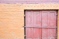 Texture of brick orange painted brown paint of an old brick wall with seams and a red wooden door locked on a bolt. The background Royalty Free Stock Photo