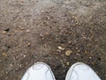 Texture macro shot of a dirt road with gravel after rain and white sneakers Royalty Free Stock Photo