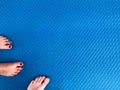 Texture with male and female feet, legs with a beautiful red manicure on the fingers stand on a blue rubber non-slip mat with a pa Royalty Free Stock Photo