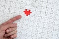 The texture of a white jigsaw puzzle in the assembled state with one missing element, forming a red space, pointed to by the finge Royalty Free Stock Photo