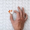 The texture of a white jigsaw puzzle in the assembled state with one missing element that the male hand puts in Royalty Free Stock Photo