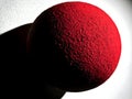 A textured red sphere casting a shadow against a light background Royalty Free Stock Photo