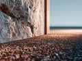 Textured stone wall meeting a pebbled ground surface with soft natural lighting creating shadows and a blurred horizon in the Royalty Free Stock Photo