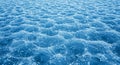 A textured surface of blue ice with a wave-like pattern, reflecting light and creating