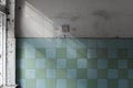 Textured wall of an abandoned building, lined with glossy square ceramic turquoise tiles with the sun\'s rays on the wall