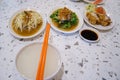 Textured of a white table with a bowl of porridge, orange chopsticks and various side dishes.