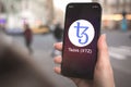 Tezos XTZ cryptocurrency symbol, logo. Business and financial concept. Hand with smartphone, screen with crypto icon