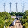 A TGV Duplex high-speed train is entering a tunnel under a row of transmission towers Royalty Free Stock Photo