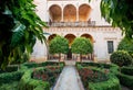 16th-century tiled gardens in the Casa de Pilatos palace with green plants and red flowers. Renaissance architecture style arches