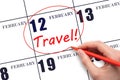 Hand drawing a red circle and writing the text TRAVEL on the calendar date 12 February. Travel planning.