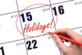 Hand drawing a red circle and writing the text Holidays on the calendar date 15July. Important date. Royalty Free Stock Photo
