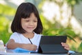 Thai Asian kid girl, aged 4 to 6 years old, looks cute, is using a tablet to study online. She sat outside in the garden at home. Royalty Free Stock Photo