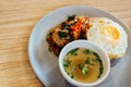 Thai basil braised pork topped with fried egg and rice along with soup on table.