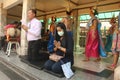 A thai couple praying at buddah temple. The woman with Corona mask. In the background: dance and music group in traditional clothe