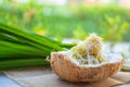 Thai dessert homemade steamed cassava cake with a fresh coconut in a coconut shell with pandan leaves blurred background on white