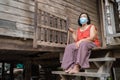 Thai elderly woman in round-necked sleeveless collar wearing medical mask for protect corona virus covid-19 pandemic in wooden