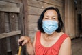 Thai elderly woman in round-necked sleeveless collar wearing medical mask for protect corona virus covid-19 pandemic in wooden