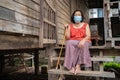 Thai elderly woman in round-necked sleeveless collar wearing medical mask for protect corona virus covid-19 pandemic in wooden