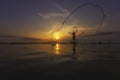 A Thai fisherman on a long tail boat casting a net to catch freshwater fish Royalty Free Stock Photo