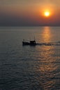 Thai fishing boat passes by the sun as it sets on Hua Hin coast Royalty Free Stock Photo