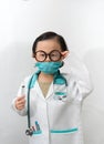 Thai kid boy with glasses and stethoscope and his hand hold syringe for injection in doctor gown or uniform with mask like Royalty Free Stock Photo