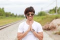 Thai male teen in sunglasses and white T-shirt is smiling and performing Thai greeting.