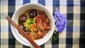 Thai noodle with stewed pork rib and mushrooms with chopsticks and purple flowerson checkered tablecloth