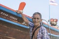 Thai old fisherman is standing near his wooden boat near the shore on the island Koh Phangan, Thailand Royalty Free Stock Photo