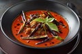 Thai red curry with black beans in black bowl on wooden tabl.