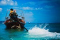 Thai Sailor fisherman on a longtail boat. Drives ship with handmade automobile engine on it. Man in orange hoodie. Sea with liner Royalty Free Stock Photo