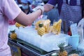 Thai street food. Woman buying small peeled and sliced pineapples at a local market.