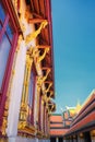 A Thai temple with a red roof, gold accents, and mythical creature statues, set against a blue sky