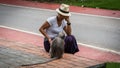 Thai woman in sarong and white fedora looking at Duskey monkey